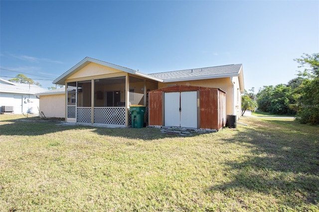 back of property with a lawn, a sunroom, an outdoor structure, a shed, and central AC