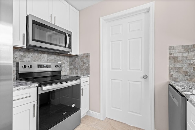 kitchen with light tile patterned flooring, appliances with stainless steel finishes, white cabinetry, decorative backsplash, and light stone counters