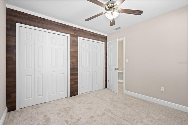 unfurnished bedroom with ceiling fan, light colored carpet, multiple closets, and wood walls