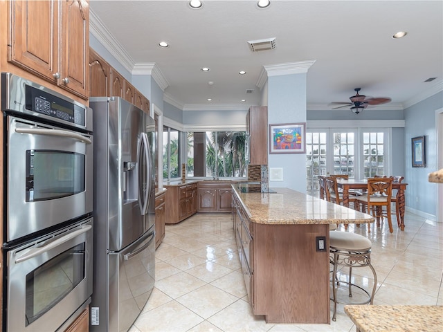 kitchen with light stone counters, ornamental molding, appliances with stainless steel finishes, and light tile patterned floors