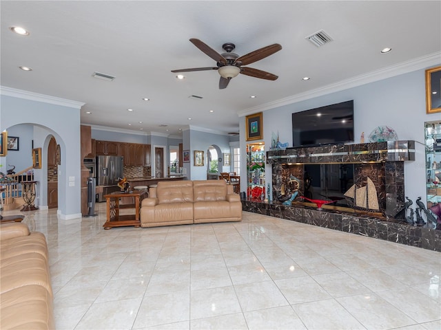 tiled living room featuring crown molding, ceiling fan, and a fireplace