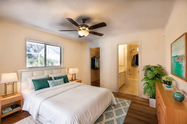 bedroom with a walk in closet, ceiling fan, dark wood-type flooring, ensuite bath, and a closet