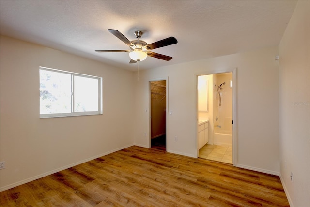 unfurnished bedroom with ensuite bathroom, light hardwood / wood-style flooring, a walk in closet, a textured ceiling, and a closet