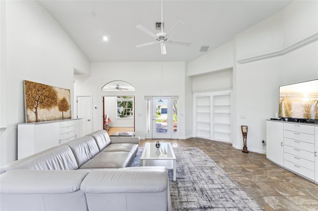 living room featuring ceiling fan, a towering ceiling, and built in shelves