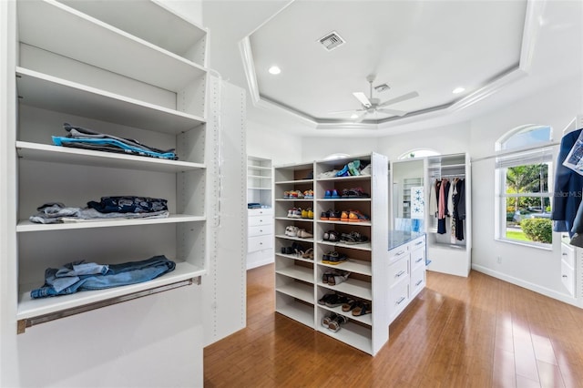 walk in closet with hardwood / wood-style floors, a raised ceiling, and ceiling fan