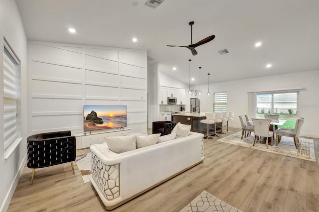 living room with vaulted ceiling, ceiling fan, and light wood-type flooring