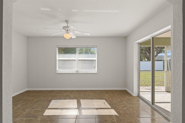 empty room featuring a textured ceiling, dark tile patterned flooring, and ceiling fan