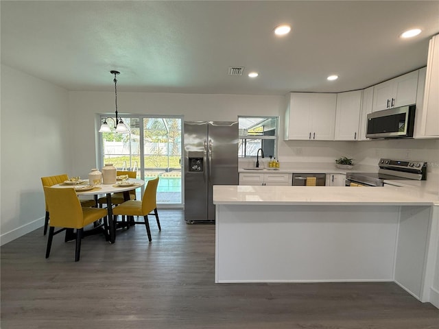 kitchen featuring visible vents, dark wood finished floors, a peninsula, stainless steel appliances, and a sink