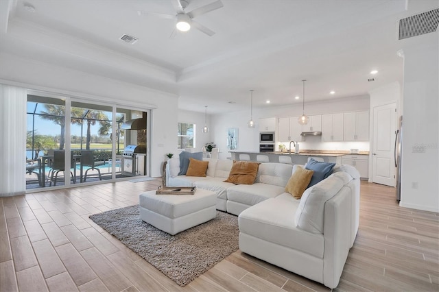 living room featuring sink, a tray ceiling, ornamental molding, and ceiling fan