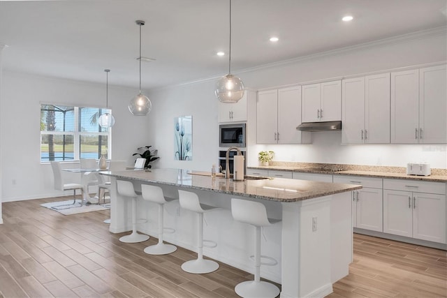 kitchen featuring built in microwave, pendant lighting, a center island with sink, and white cabinets