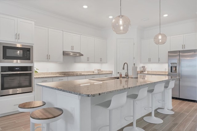 kitchen with pendant lighting, appliances with stainless steel finishes, a kitchen island with sink, and white cabinets