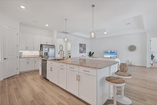 kitchen featuring white cabinetry, decorative light fixtures, appliances with stainless steel finishes, light stone countertops, and a kitchen island with sink