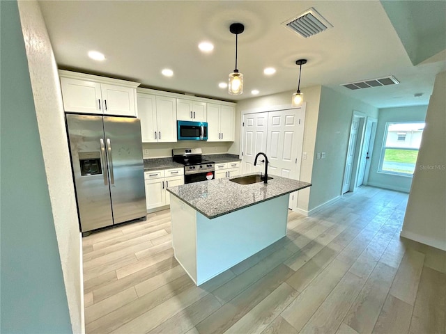 kitchen with white cabinetry, sink, dark stone counters, stainless steel appliances, and light hardwood / wood-style flooring