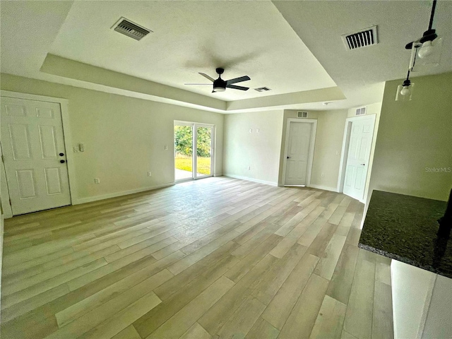 interior space with a raised ceiling, ceiling fan, and light wood-type flooring