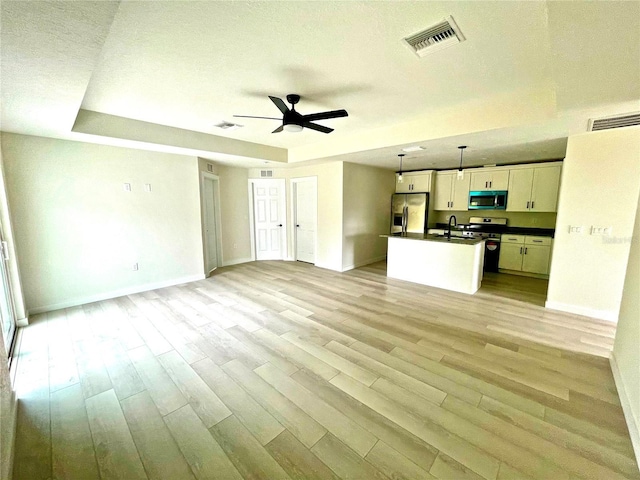 unfurnished living room featuring sink, ceiling fan, light hardwood / wood-style floors, a textured ceiling, and a raised ceiling