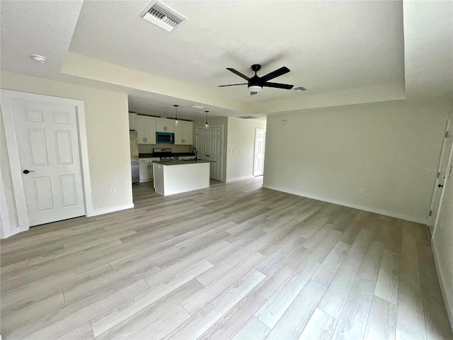 unfurnished living room featuring sink, light hardwood / wood-style flooring, ceiling fan, a textured ceiling, and a raised ceiling