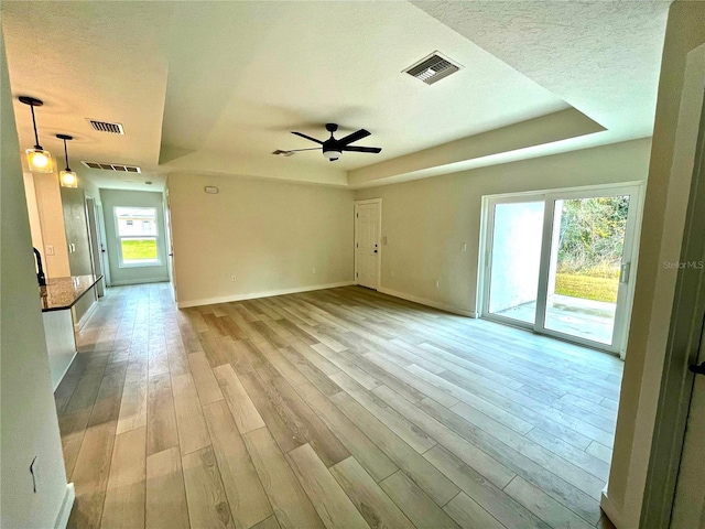 spare room with ceiling fan, a raised ceiling, light hardwood / wood-style flooring, and a textured ceiling