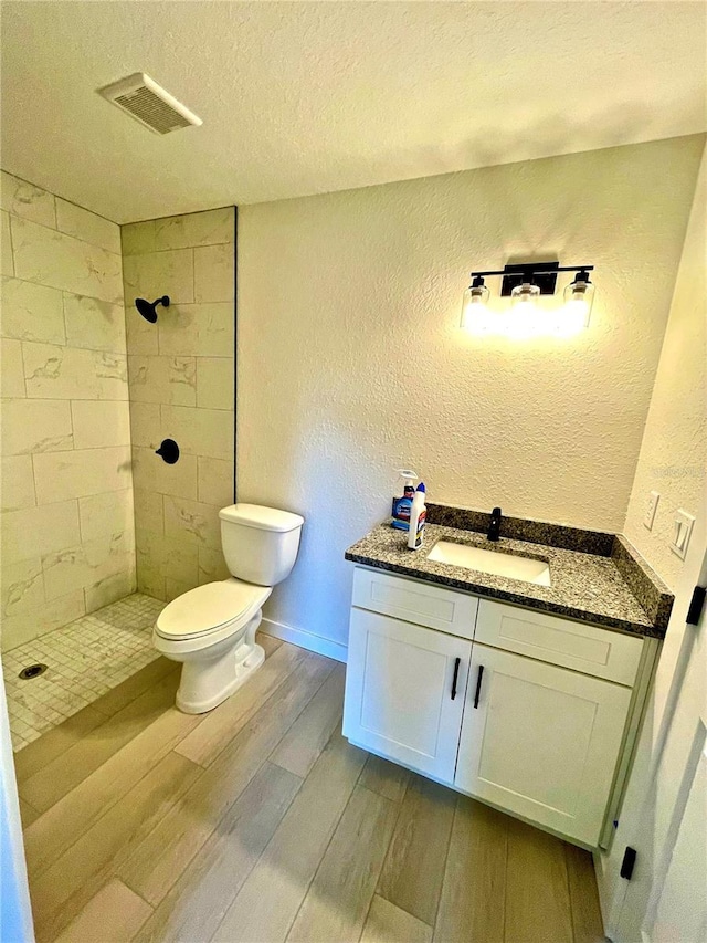 bathroom featuring toilet, wood-type flooring, a textured ceiling, a tile shower, and vanity