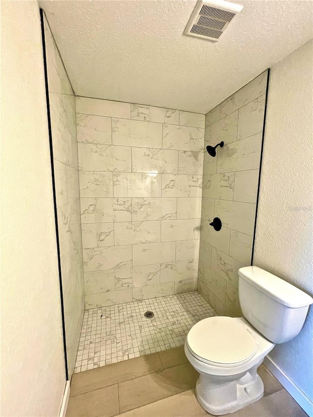 bathroom with tiled shower, a textured ceiling, and toilet