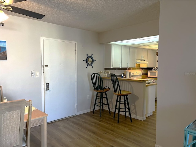 kitchen featuring white cabinetry, a kitchen breakfast bar, kitchen peninsula, light hardwood / wood-style floors, and decorative backsplash