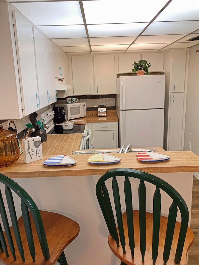 kitchen with a peninsula, white appliances, and white cabinetry