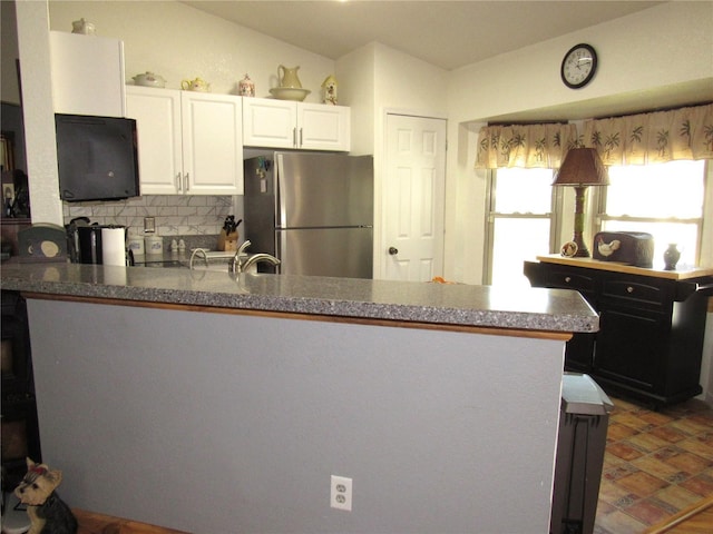 kitchen featuring lofted ceiling, stainless steel refrigerator, backsplash, white cabinets, and kitchen peninsula