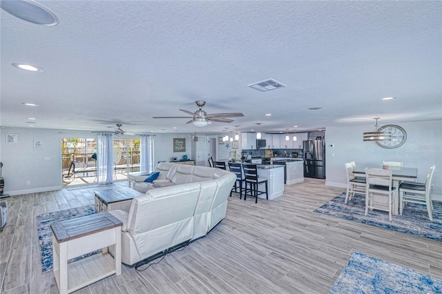 living room featuring ceiling fan with notable chandelier, light hardwood / wood-style flooring, and a textured ceiling