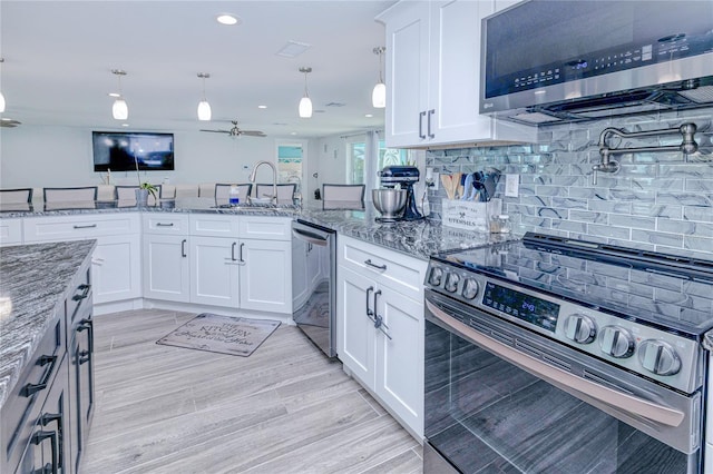 kitchen with decorative light fixtures, white cabinetry, sink, light stone counters, and stainless steel appliances