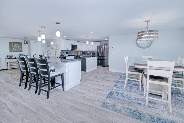 kitchen with pendant lighting, light stone countertops, stainless steel appliances, and white cabinets