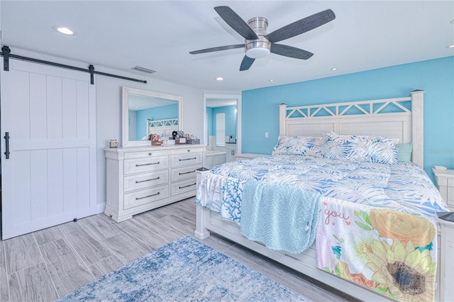 bedroom featuring ceiling fan, a barn door, and light hardwood / wood-style floors