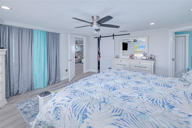 bedroom featuring a barn door, ceiling fan, and light wood-type flooring