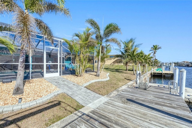 view of dock with a water view, a yard, and glass enclosure