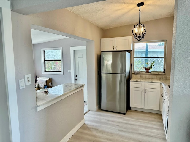 kitchen with stainless steel fridge, white cabinetry, hanging light fixtures, a healthy amount of sunlight, and light wood-type flooring