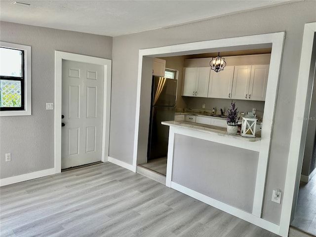 kitchen featuring white cabinetry, an inviting chandelier, refrigerator, and light hardwood / wood-style flooring