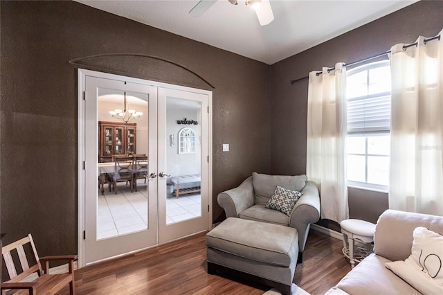 living area featuring french doors, wood-type flooring, and ceiling fan with notable chandelier