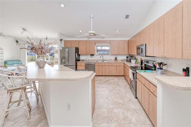 kitchen featuring sink, stainless steel appliances, a kitchen breakfast bar, vaulted ceiling, and light brown cabinets