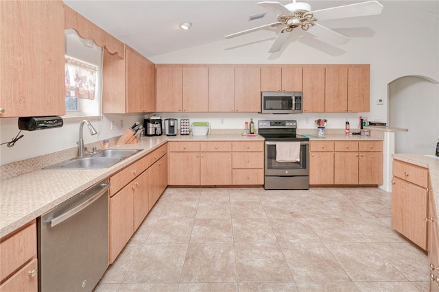 kitchen with sink, ceiling fan, appliances with stainless steel finishes, light brown cabinetry, and vaulted ceiling