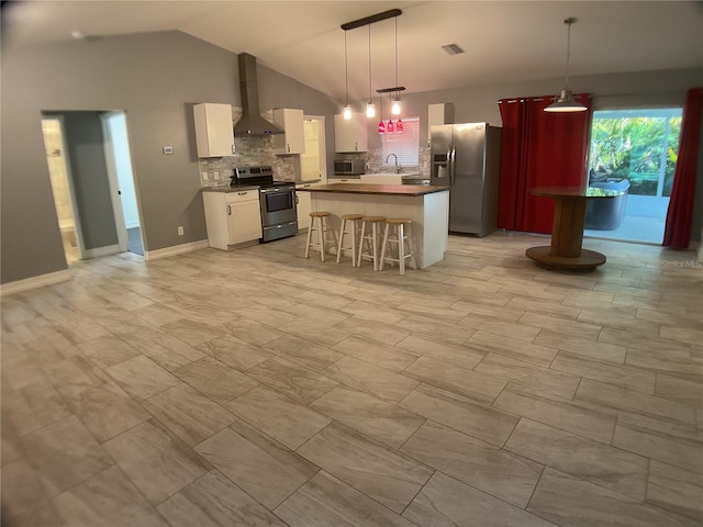 kitchen featuring decorative light fixtures, appliances with stainless steel finishes, a kitchen breakfast bar, white cabinets, and wall chimney range hood