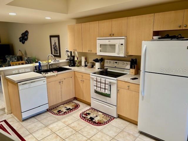 kitchen with light tile patterned floors, light countertops, light brown cabinetry, a sink, and white appliances