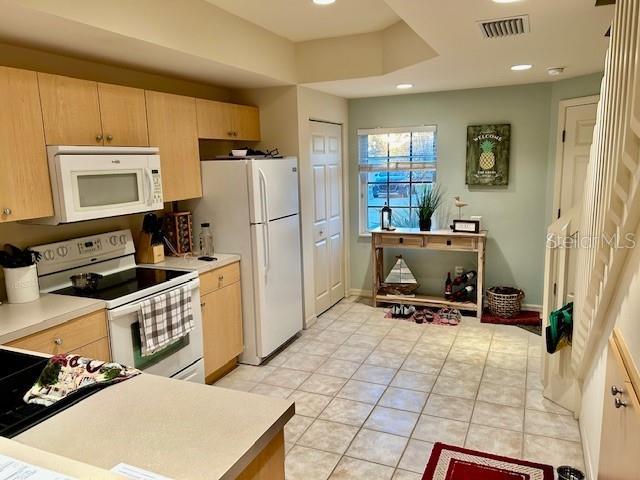 kitchen featuring light tile patterned floors, white appliances, visible vents, light countertops, and light brown cabinetry