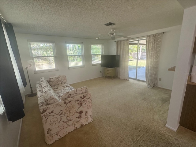 living area with ceiling fan, light colored carpet, and a textured ceiling