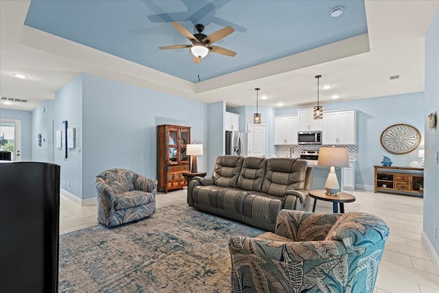 living room with a raised ceiling, ceiling fan, and light tile patterned flooring