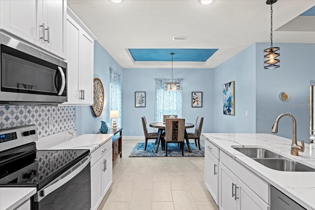 kitchen with hanging light fixtures, a tray ceiling, stainless steel appliances, and sink