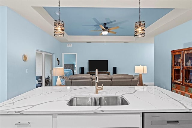 kitchen featuring pendant lighting, sink, a raised ceiling, and a center island with sink