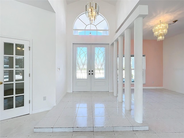 tiled entryway featuring a towering ceiling, a notable chandelier, and french doors