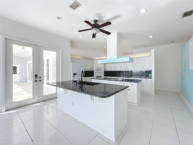 kitchen with island range hood, sink, white cabinets, white fridge with ice dispenser, and a center island with sink