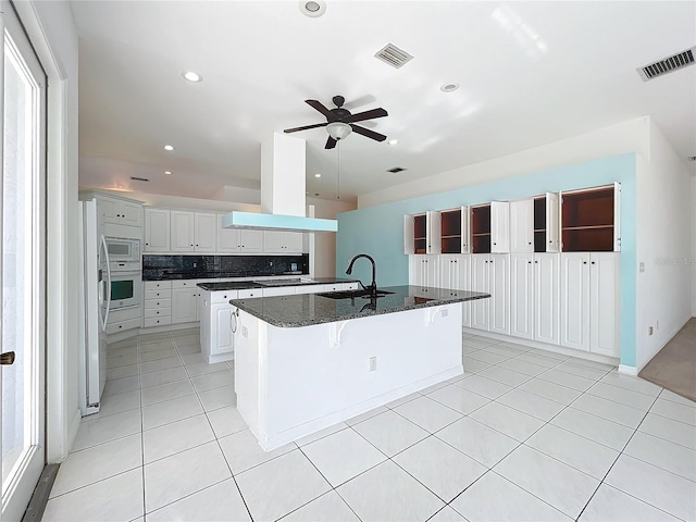 kitchen featuring white cabinetry, an island with sink, sink, dark stone counters, and island exhaust hood