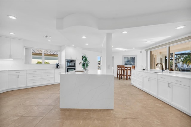 kitchen featuring sink, white cabinetry, light stone counters, light tile patterned floors, and stainless steel double oven