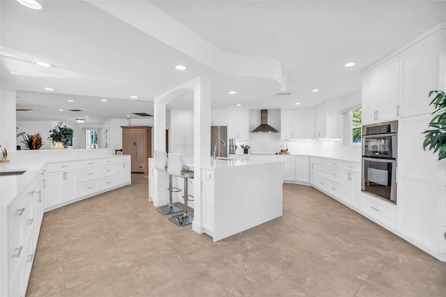 kitchen with a kitchen island with sink, white cabinets, wall chimney exhaust hood, and appliances with stainless steel finishes