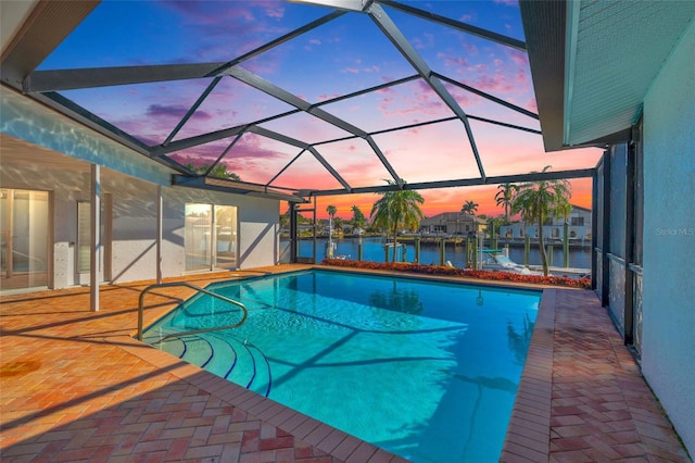 pool at dusk featuring a patio area, glass enclosure, and a water view